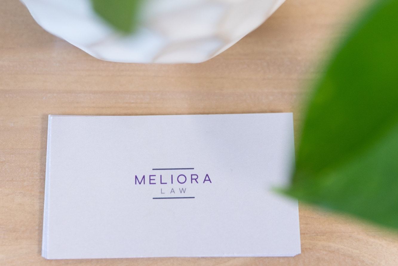 A Meliora Law card on the desk, plant leaves in the foreground